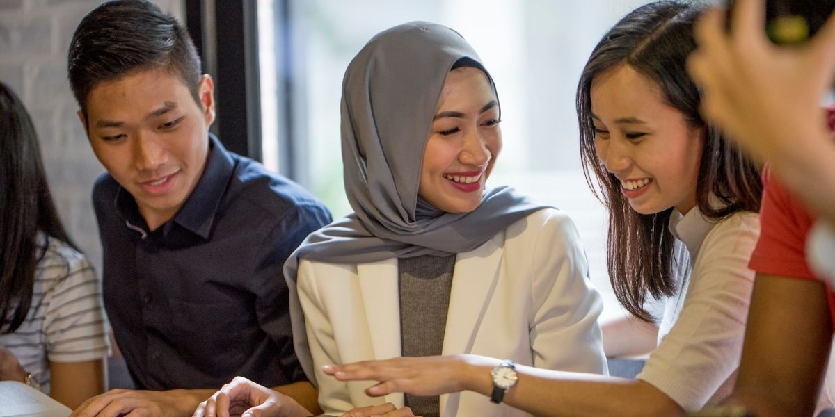 Three diverse professionals, including a woman wearing a hijab, smiling and collaborating together over a document