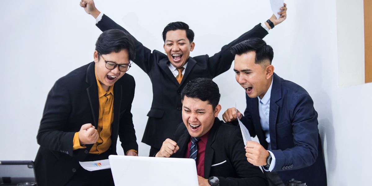 Four excited professionals in business suits cheering and celebrating a success around a laptop